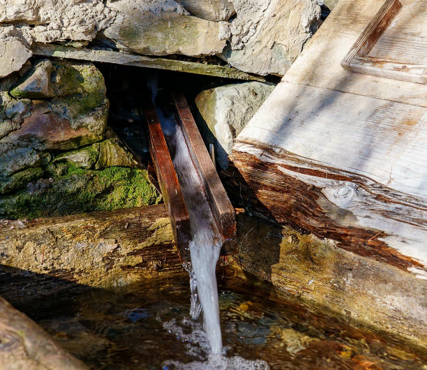 Alpine spring water running from a wooden spout into a stone trough