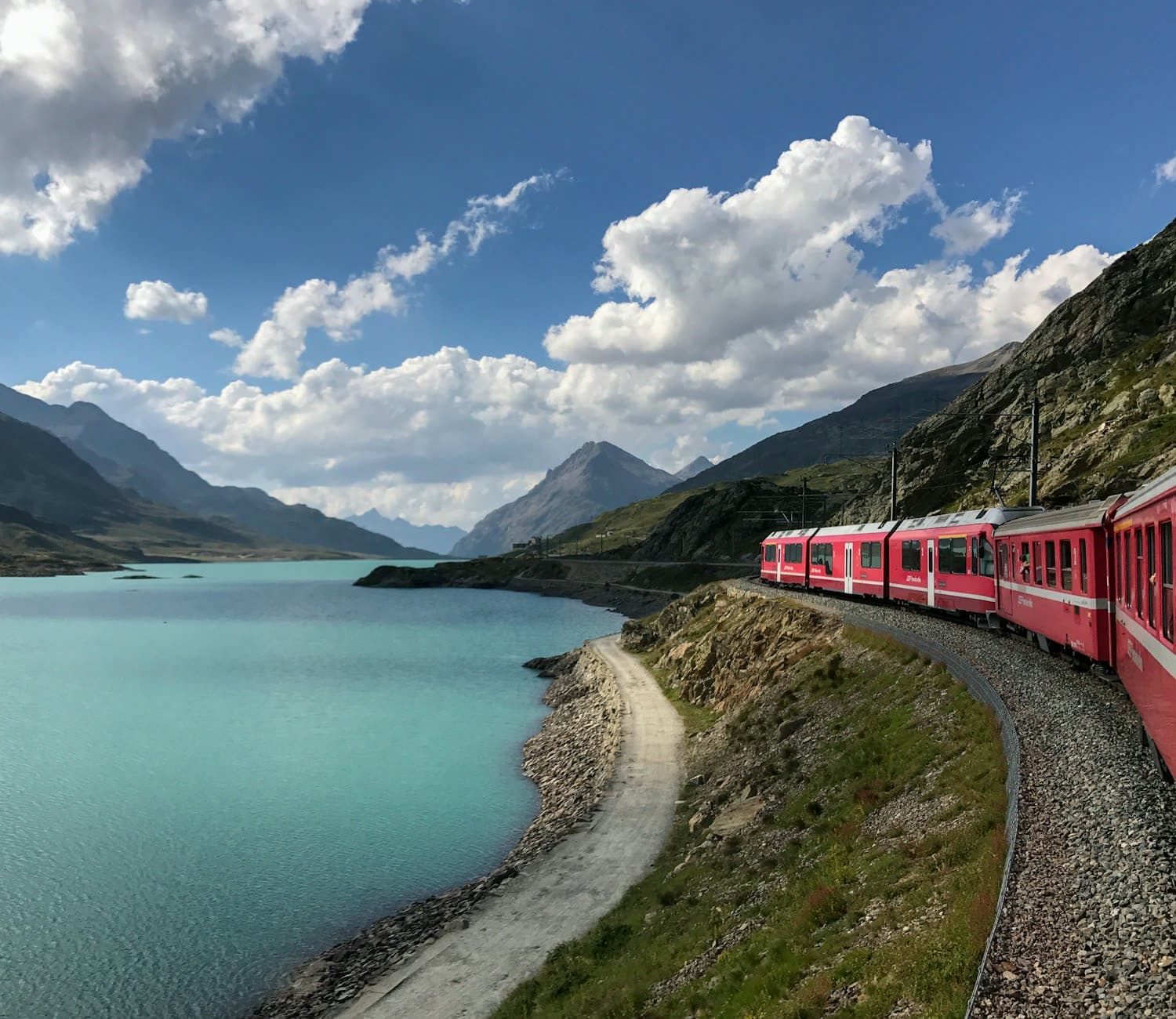 A red alpine train curving along a turquoise mountain lake